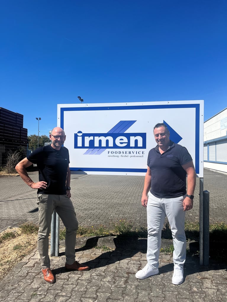 Rainer Laabs von der GILDE und Oliver Irmen von Foodservice Irmen stehen vor dem Firmenschild auf dem Unternehmensgelände von Foodservice Irmen in Trier